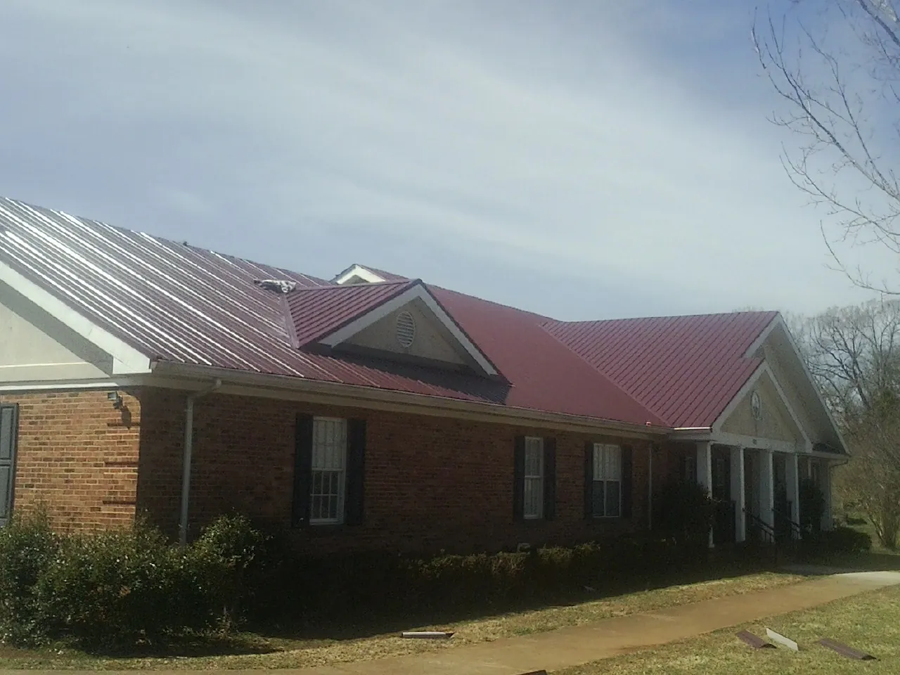 Red metal roof with gabled entries on a long brick building, from a Hail Damage Roof Repair job in Milton